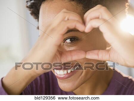 Stock Photograph - Close up portrait of Black woman forming heart-shape with hands. Fotosearch
