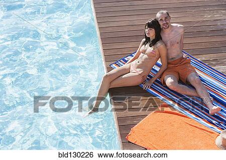 Couple relaxing together by swimming pool View Large Photo Image Stock Photograph - Couple relaxing together by swimming pool. Fotosearch
