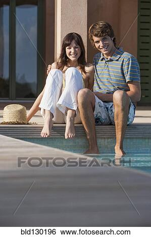 Couple sitting by swimming pool View Large Photo Image Stock Photograph - Couple sitting by swimming pool. Fotosearch