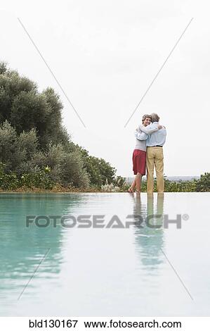 Stock Photo - Couple standing by infinity pool. Fotosearch