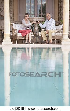 Stock Image - Couple toasting each other by swimming pool. Fotosearch