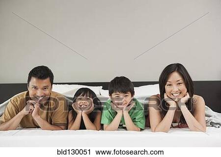Stock Image - Family laying together on bed. Fotosearch