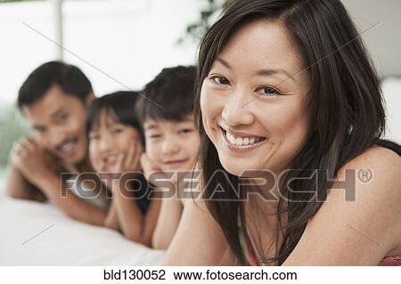 Stock Image - Family laying together on bed. Fotosearch