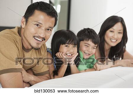 Stock Image - Family laying together on bed. Fotosearch