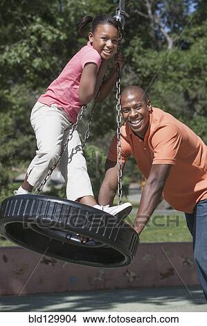 Picture - Father and daughter playing on tire swing. Fotosearch
