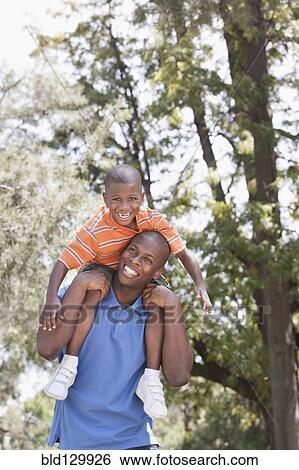 Father carrying son on shoulders in park View Large Photo Image Stock Photograph - Father carrying son on shoulders in park. Fotosearch