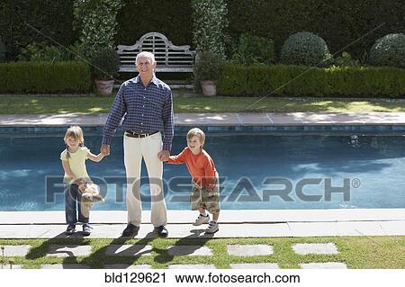 Stock Image - Grandfather and grandchildren standing at poolside. Fotosearch