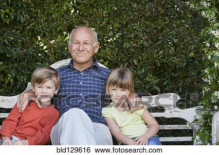 Stock Photograph - Grandfather sitting with grandchildren on garden bench. Fotosearch