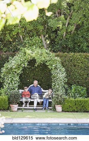 Stock Photography - Grandfather sitting with grandchildren on garden bench. Fotosearch