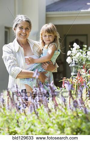Stock Image - Grandmother and granddaughter admiring flowers. Fotosearch