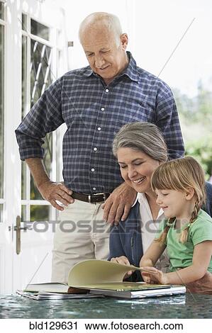 Stock Image - Grandparents and granddaughter reading outdoors. Fotosearch