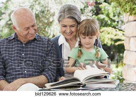Stock Photograph - Grandparents and granddaughter reading outdoors. Fotosearch