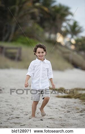 Stock Image - Hispanic boy walking on beach. Fotosearch