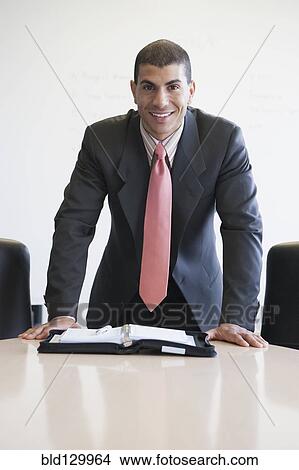 Picture - Hispanic businessman standing at conference table. Fotosearch