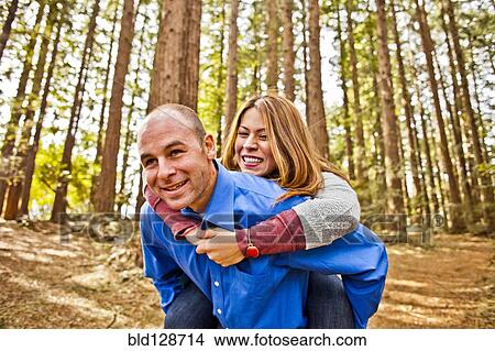 Hispanic man carrying girlfriend piggy back in forest View Large Photo Image Picture - Hispanic man carrying girlfriend piggy back in forest. Fotosearch
