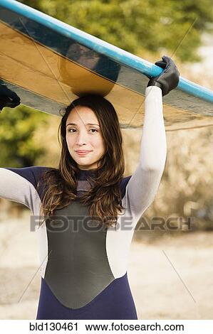 Stock Image - Hispanic surfer carrying board on beach. Fotosearch
