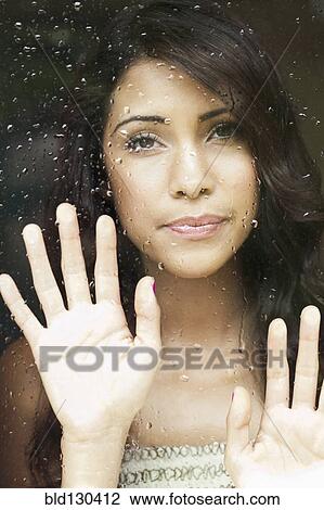 Stock Image - Hispanic woman looking out rainy window. Fotosearch