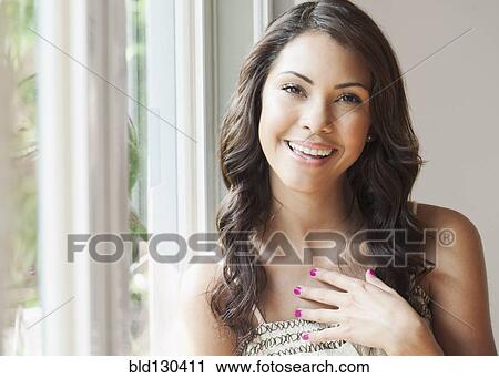 Stock Image - Hispanic woman smiling by window. Fotosearch