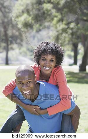 Stock Photo - Man carrying girlfriend piggyback in park. Fotosearch