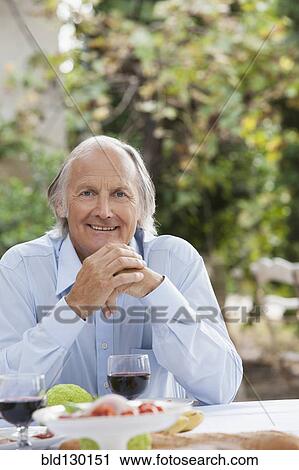 Stock Image - Man eating at table outdoors. Fotosearch