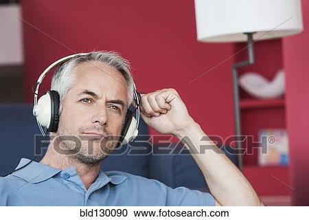 Stock Image - Man listening to headphones in living room. Fotosearch