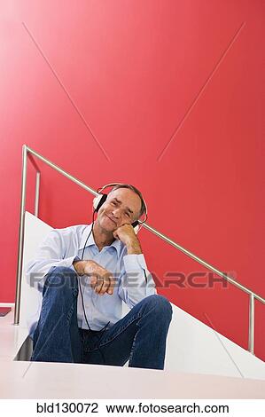 Stock Image - Man listening to headphones on stairs. Fotosearch