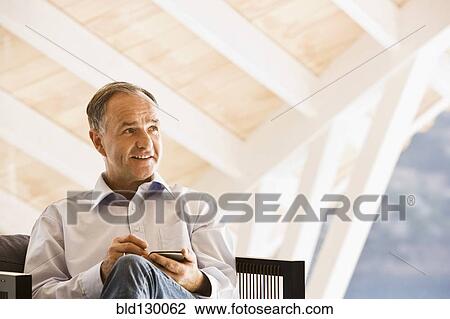 Stock Image - Man using cell phone in armchair. Fotosearch