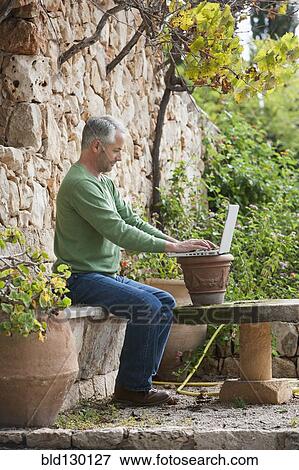 Stock Photo - Man using laptop in backyard. Fotosearch