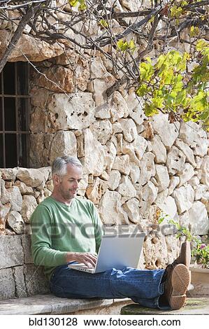 Stock Photo - Man using laptop in backyard. Fotosearch