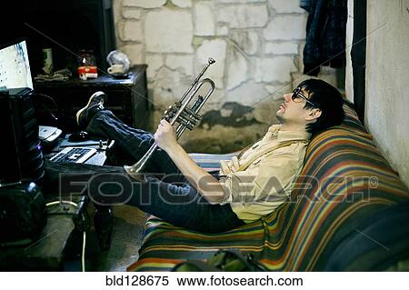Stock Photography - Mari man holding trumpet on sofa. Fotosearch