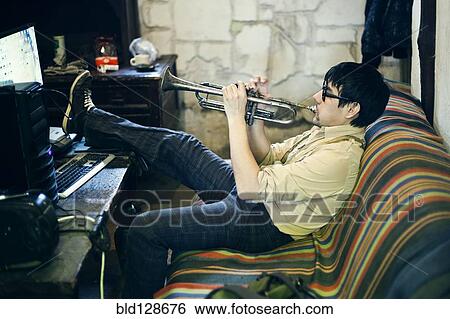 Stock Photograph - Mari man playing trumpet on sofa. Fotosearch