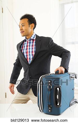 Stock Image - Mixed race businessman carrying suitcase. Fotosearch