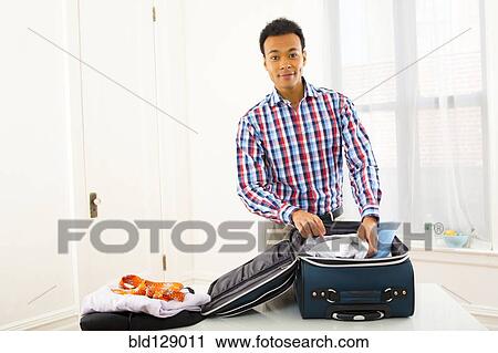 Stock Image - Mixed race businessman packing suitcase. Fotosearch