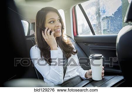 Stock Photograph - Mixed race businesswoman talking on cell phone in taxi. Fotosearch