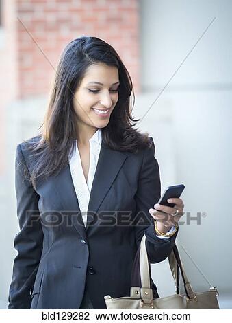 Stock Image - Mixed race businesswoman using cell phone on city street. Fotosearch