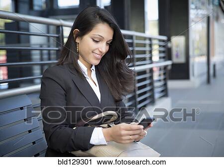 Stock Image - Mixed race businesswoman using cell phone on train platform. Fotosearch
