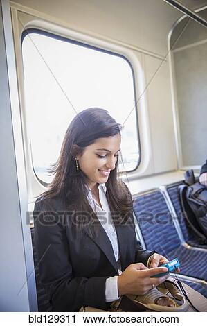 Stock Image - Mixed race businesswoman using cell phone on train. Fotosearch