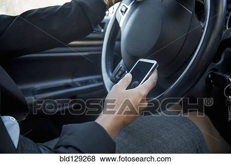 Stock Photo - Mixed race businesswoman using cell phone while driving. Fotosearch