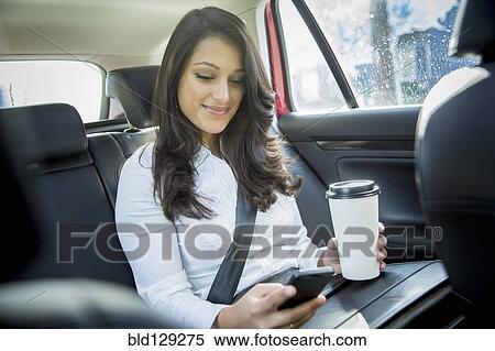 Stock Photography - Mixed race businesswoman using cell phone in taxi. Fotosearch