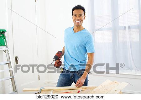 Stock Image - Mixed race carpenter holding power drill. Fotosearch