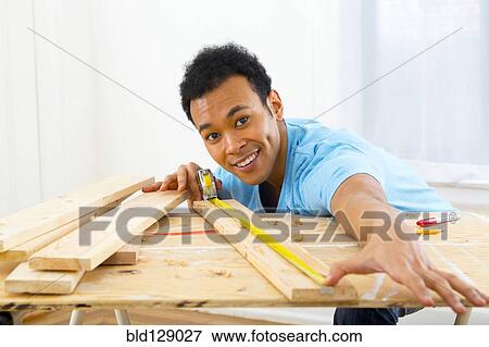 Stock Photo - Mixed race carpenter measuring wood with tape measure. Fotosearch