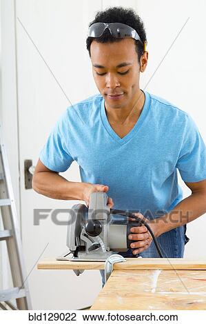 Stock Image - Mixed race carpenter using hand saw. Fotosearch