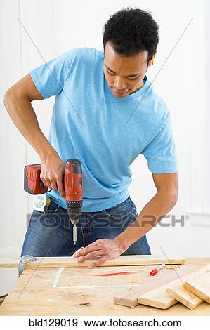 Stock Photo - Mixed race carpenter using power drill. Fotosearch