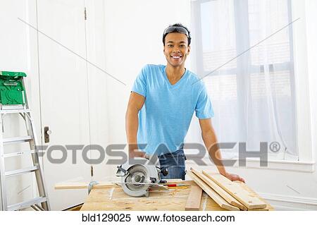 Stock Photography - Mixed race carpenter with hand saw. Fotosearch