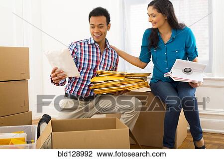 Stock Image - Mixed race couple packing cardboard boxes. Fotosearch