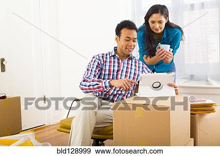 Mixed race couple using digital tablet in new home View Large Photo Image Stock Photo - Mixed race couple using digital tablet in new home. Fotosearch