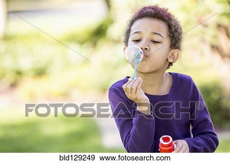 Stock Photo - Mixed race girl blowing bubbles outdoors. Fotosearch