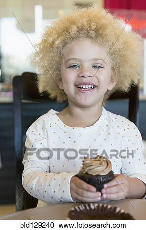 Stock Image - Mixed race girl having cupcake in bakery. Fotosearch