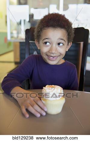 Stock Photo - Mixed race girl having cupcake in bakery. Fotosearch
