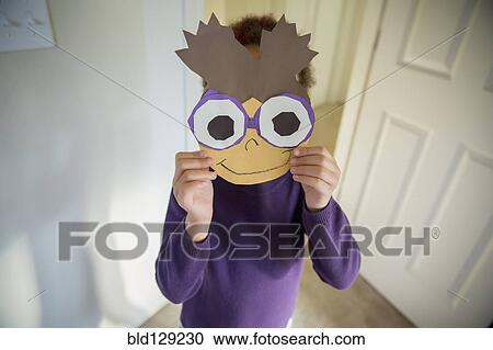 Stock Image - Mixed race girl holding mask over face. Fotosearch